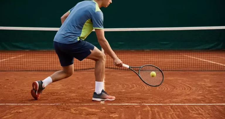 Männlicher Tennisspieler bei einem Stoppball am Netz auf rotem Sandplatz, dynamische Athletik-Pose mit Tennisschläger