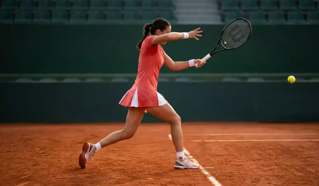 Weibliche Tennisspielerin bei einer Topspin-Vorhand auf rotem Sandplatz, dynamische Athletik-Pose mit modernem Schläger