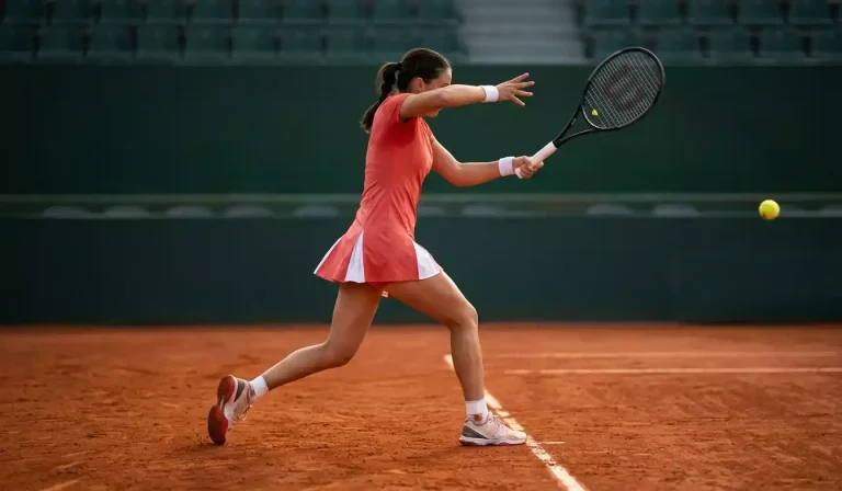 Weibliche Tennisspielerin bei einer Topspin-Vorhand auf rotem Sandplatz, dynamische Athletik-Pose mit modernem Schläger